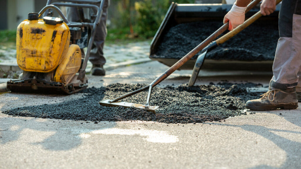 A person using a rake to cover a hole in the road with new asphalt for an asphalt repair in El Paso.