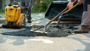 A person using a rake to cover a hole in the road with new asphalt for an asphalt repair in El Paso.