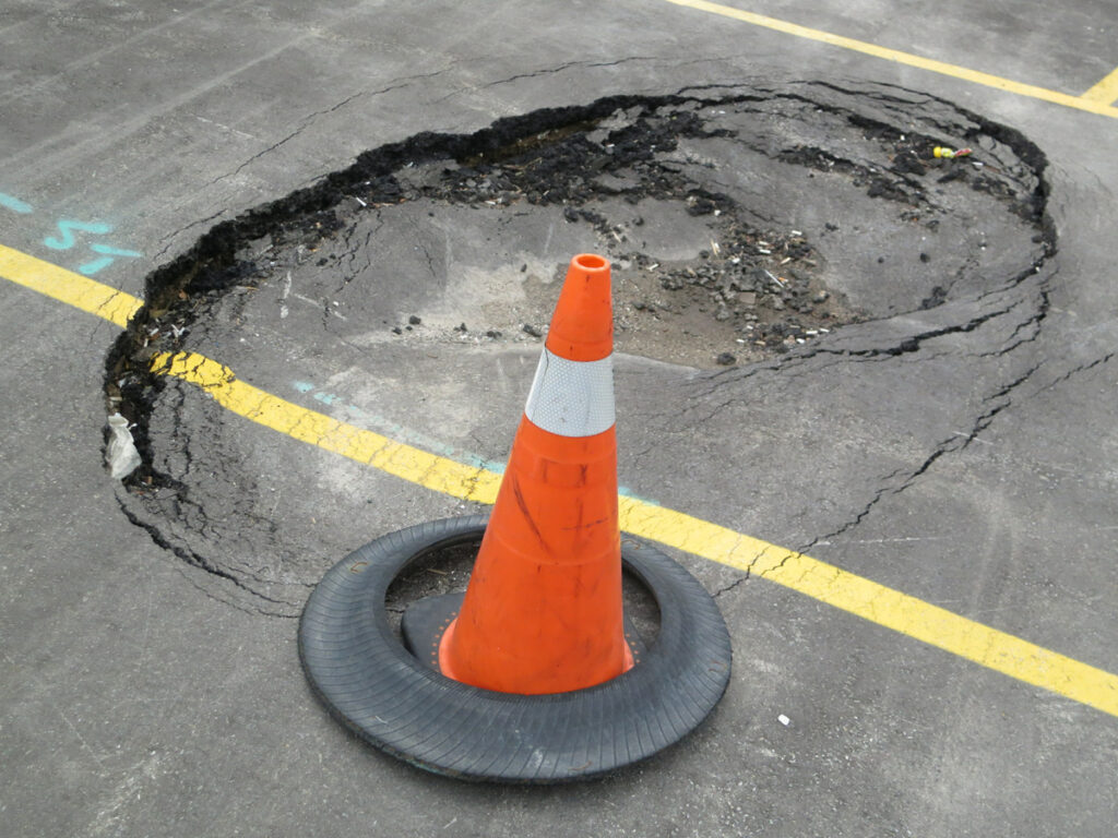A pothole in a parking lot with an orange caution cone in front of it in El Paso.