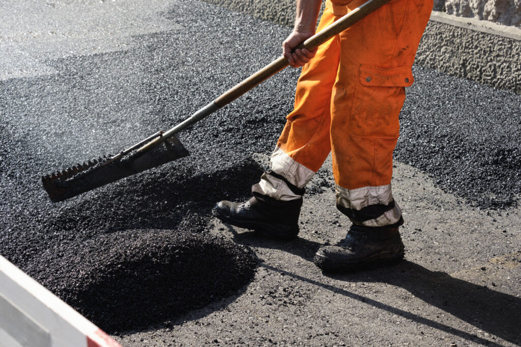 A person in orange pants laying down asphalt in El Paso.