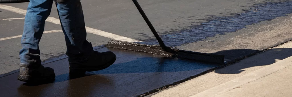 Worker using a sealcoating brush during asphalt resurfacing project in El Paso